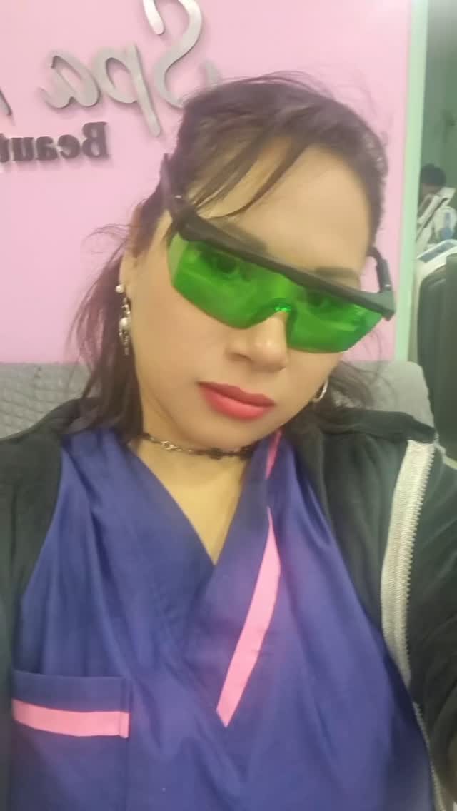 Con gafas de protección láser verdes y ambo azul con vivos rosas, delante del cartel de Spa Moment en la pared rosa